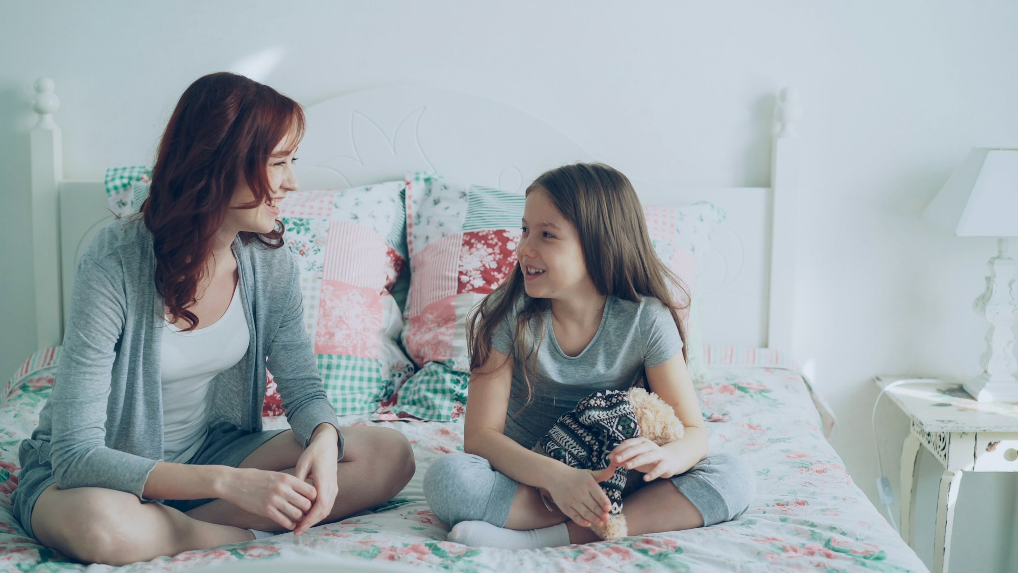 A young girl mid-sentence, talking with her mother on a bed
