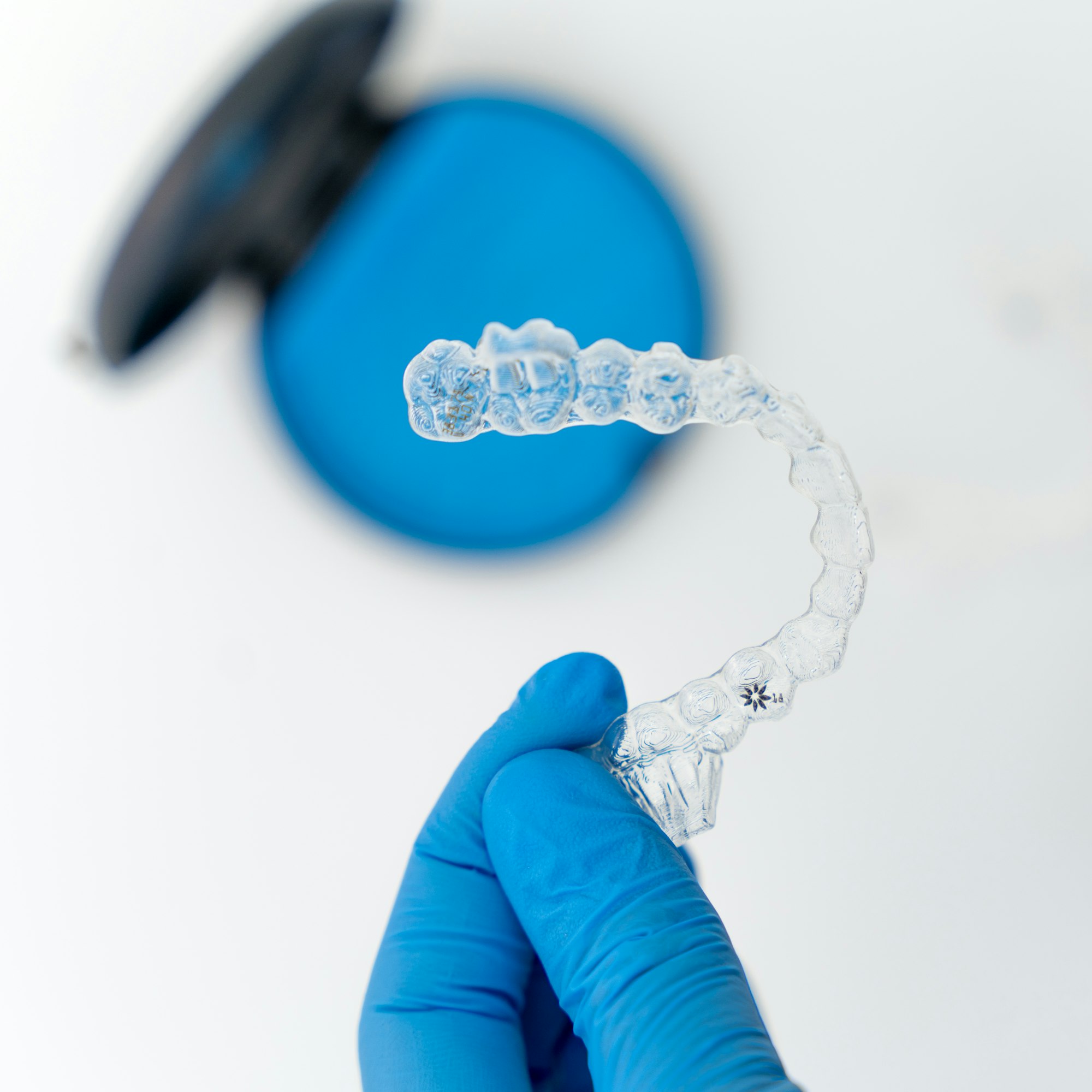 A gloved hand holding a clear removable retainer beside its case