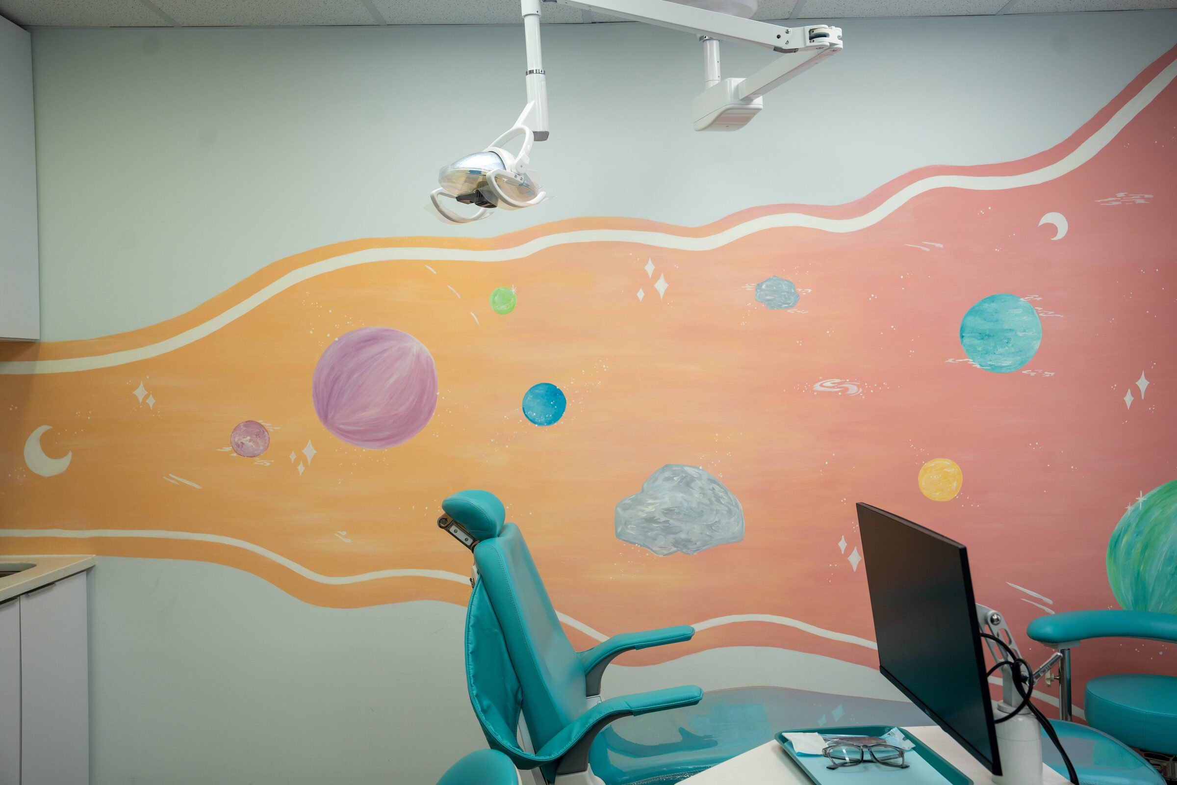 A treatment chair beside the painted planets mural