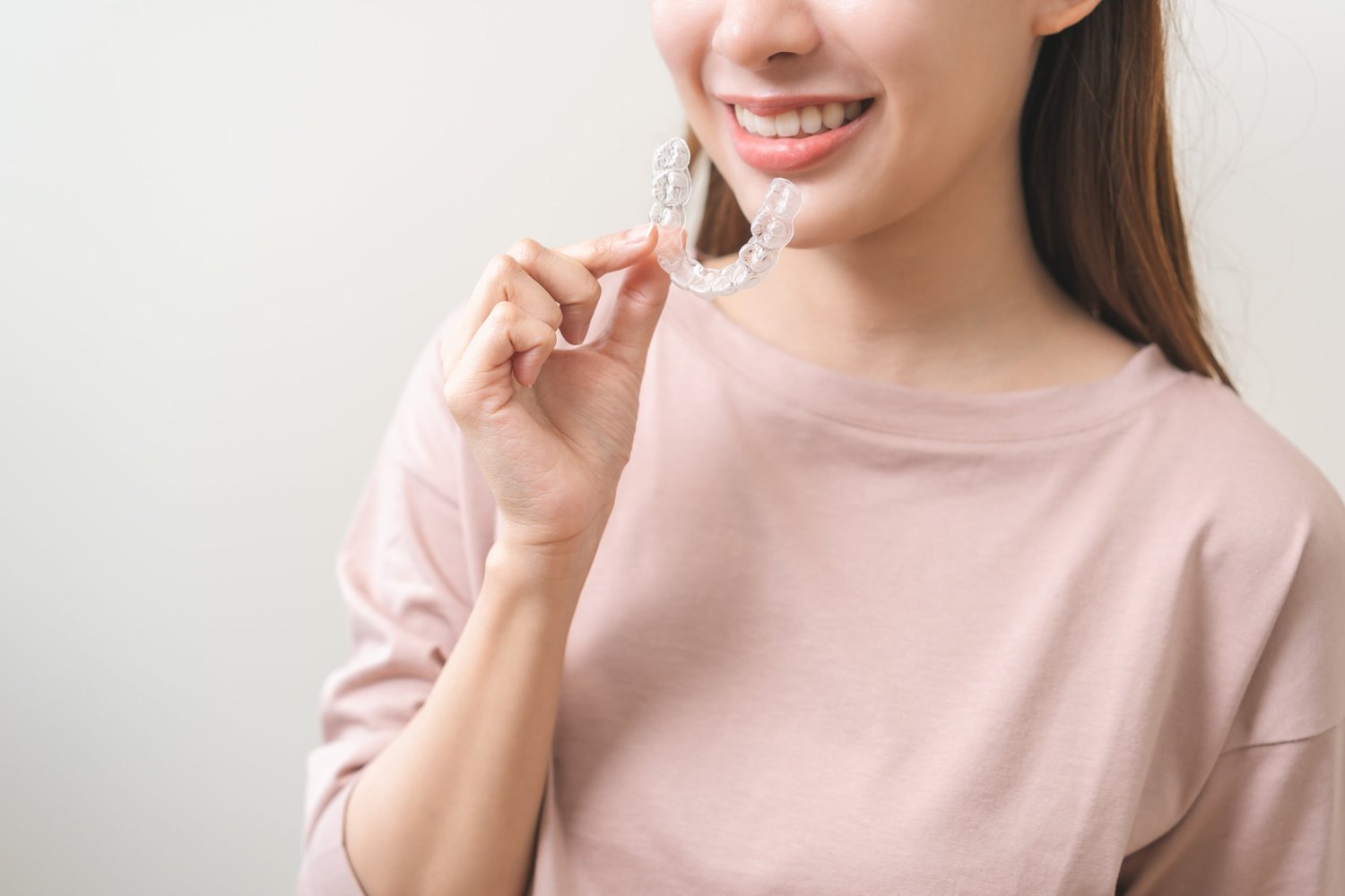A woman smiling as she holds a clear aligner